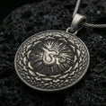 Load image into Gallery viewer, Oxidized Om pendant with circular mandala design, radiant center, and layered sacred pattern displayed on dark volcanic rock in a close-up luxury jewelry composition
