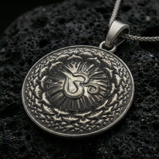 Oxidized Om pendant with circular mandala design, radiant center, and layered sacred pattern displayed on dark volcanic rock in a close-up luxury jewelry composition