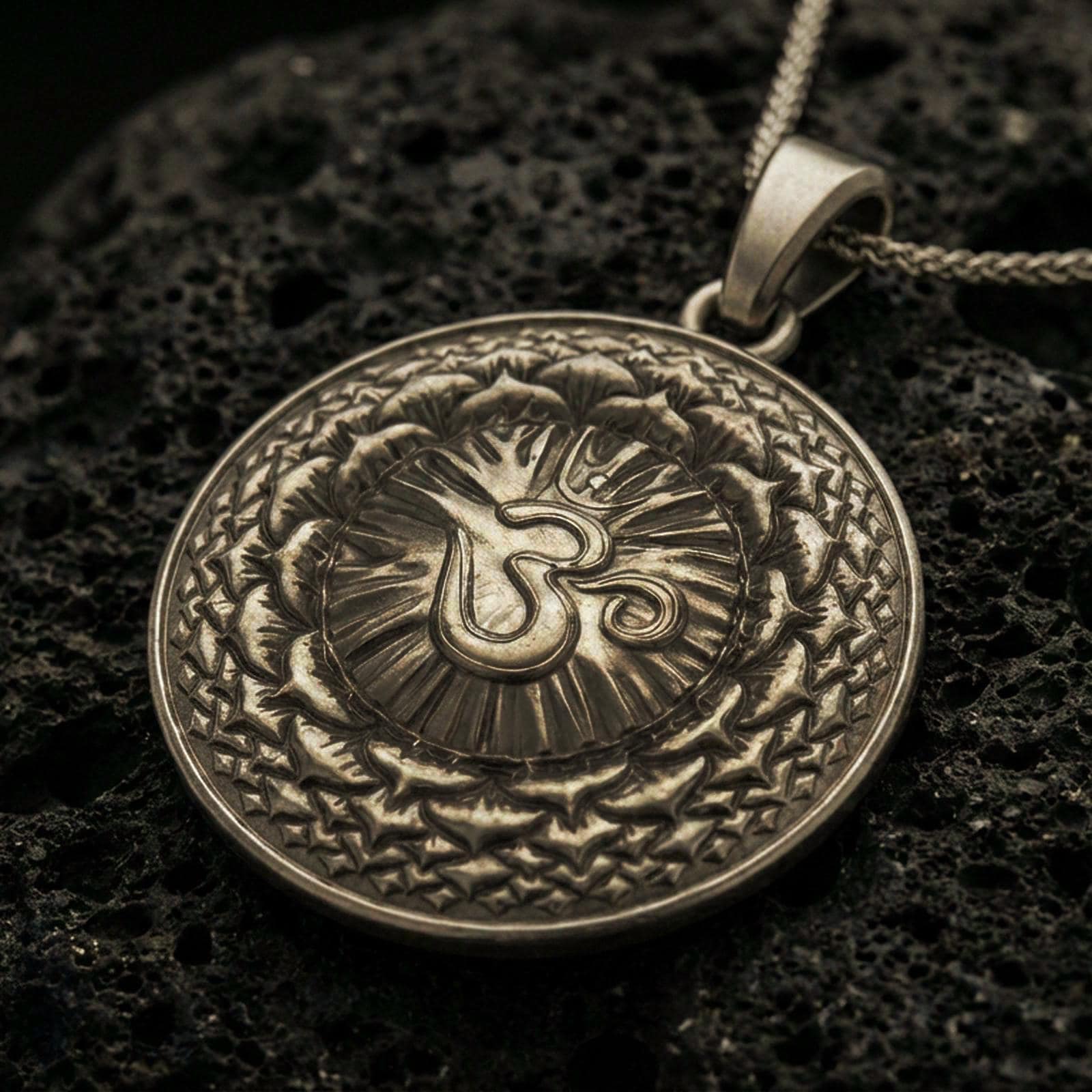 Bronze Om pendant with circular mandala design, radiant center, and layered sacred pattern displayed on dark volcanic rock in a close-up luxury jewelry composition
