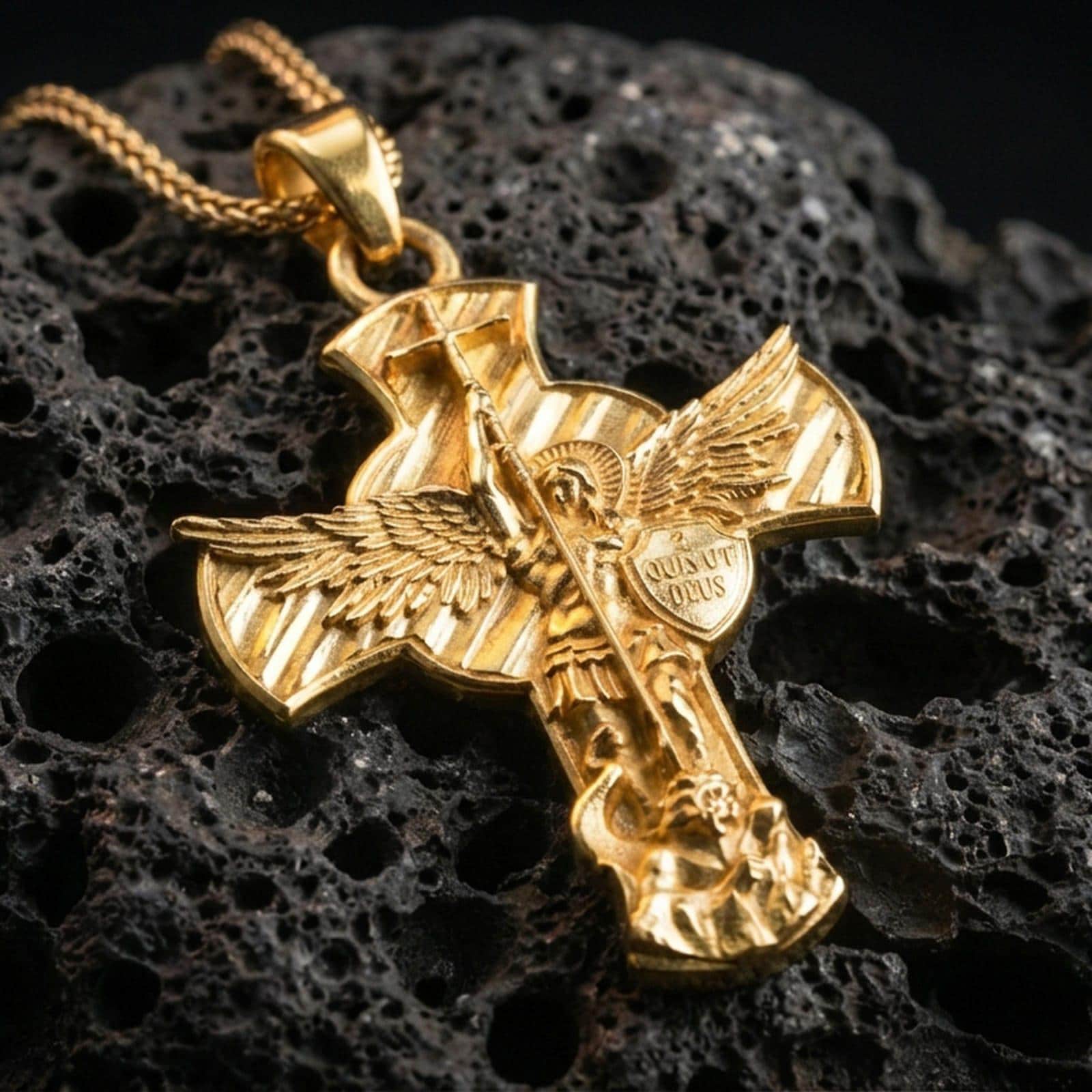 Gold plated Saint Michael pendant with angel warrior motif, Quis Ut Deus inscription, and triumphant battle scene showcased on black volcanic rock in a refined macro jewelry image