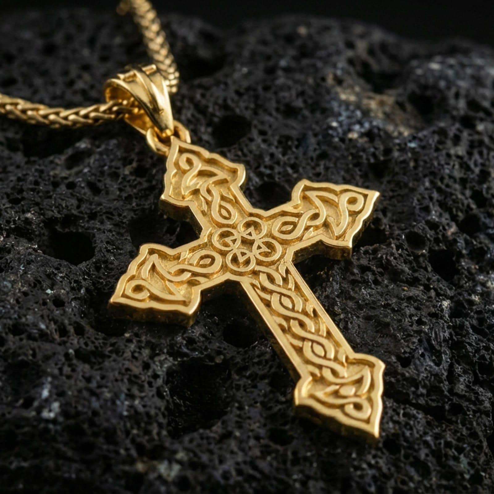 Gold plated Celtic cross pendant with continuous knot motif, decorative open structure, and elongated symbolic form showcased on black volcanic rock in a refined macro jewelry image