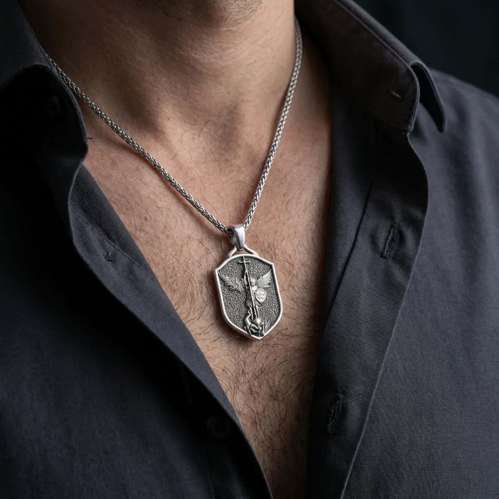 Oxidized Saint Michael shield pendant necklace worn on the neck, styled in a dark lifestyle portrait with an open shirt and masculine presentation.