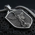 Load image into Gallery viewer, Sterling silver Saint Michael shield pendant necklace with an oxidized finish resting on textured volcanic rock, captured in a close-up premium studio composition.
