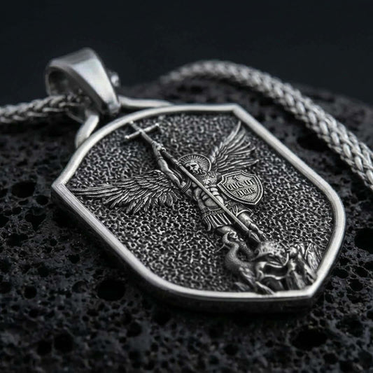 Sterling silver Saint Michael shield pendant necklace with an oxidized finish resting on textured volcanic rock, captured in a close-up premium studio composition.