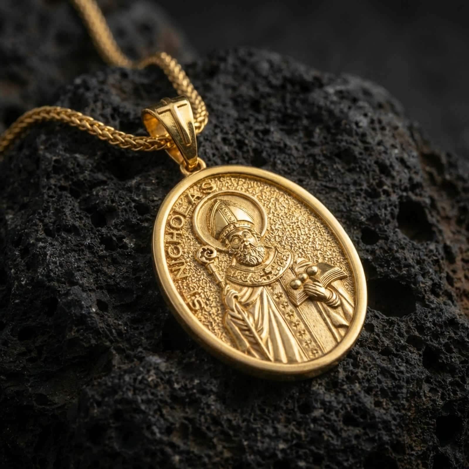 Gold plated Saint Nicholas pendant necklace presented on porous volcanic rock, highlighting the oval medallion form and sacred devotional design in a luxurious close-up jewelry image.