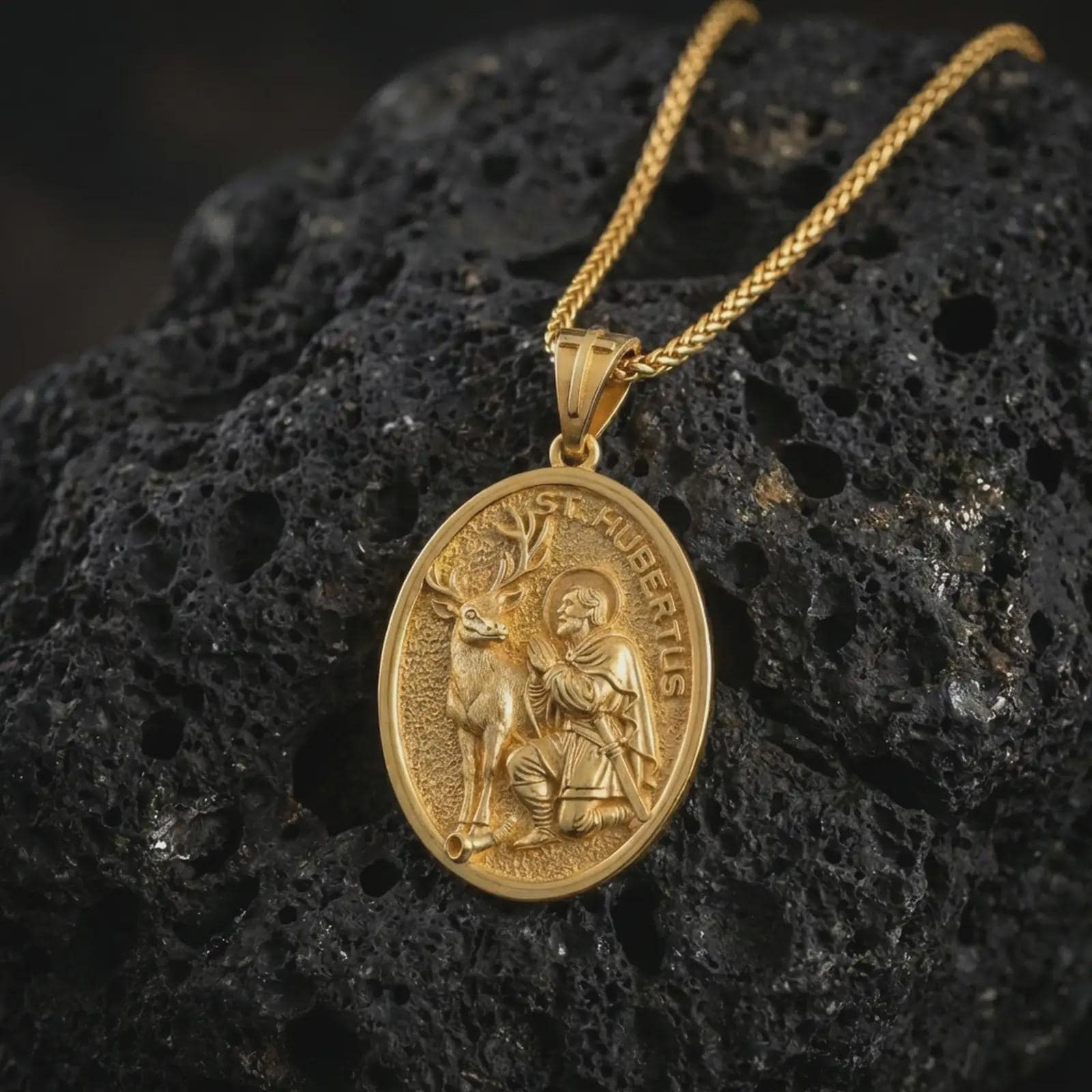 Gold plated Saint Hubert pendant necklace presented on porous volcanic rock, highlighting the oval medallion form and sacred patron design in a luxurious close-up jewelry image.