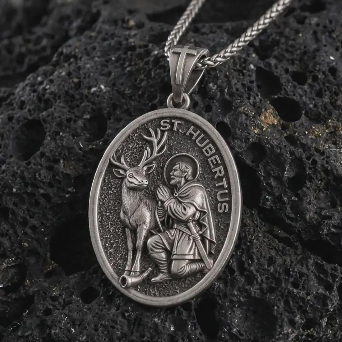 Sterling silver Saint Hubert pendant necklace with an oxidized finish resting on textured volcanic rock, captured in a close-up premium studio composition.