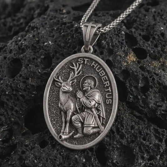 Sterling silver Saint Hubert pendant necklace with an oxidized finish resting on textured volcanic rock, captured in a close-up premium studio composition.