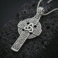 Load image into Gallery viewer, Polished silver Celtic cross pendant necklace displayed on black volcanic rock, shown in a refined macro product shot with Trinity knot and circular halo detail.
