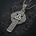 Load image into Gallery viewer, Sterling silver Celtic cross pendant necklace with an oxidized finish resting on textured volcanic rock, captured in a close-up premium studio composition.
