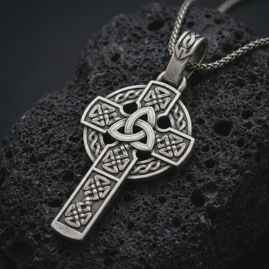 Sterling silver Celtic cross pendant necklace with an oxidized finish resting on textured volcanic rock, captured in a close-up premium studio composition.