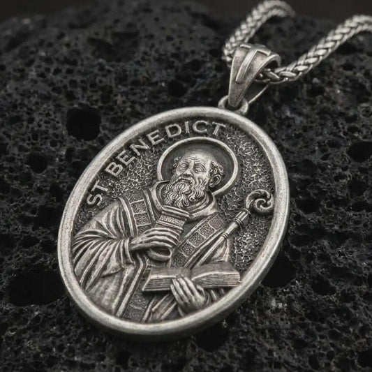 Sterling silver Saint Benedict pendant necklace with an oxidized finish resting on textured volcanic rock, captured in a close-up premium studio composition.