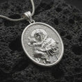 Load image into Gallery viewer, Polished silver Saint Anthony pendant necklace displayed on black volcanic rock, shown in a refined macro product shot with detailed saint and child relief.
