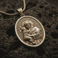 Load image into Gallery viewer, Bronze Saint Anthony pendant necklace with an oxidized finish resting on textured volcanic rock, captured in a close-up premium studio composition.
