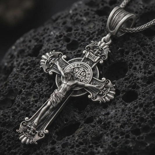 Sterling silver Saint Benedict crucifix necklace with an oxidized finish resting on textured volcanic rock, captured in a close-up premium studio composition.