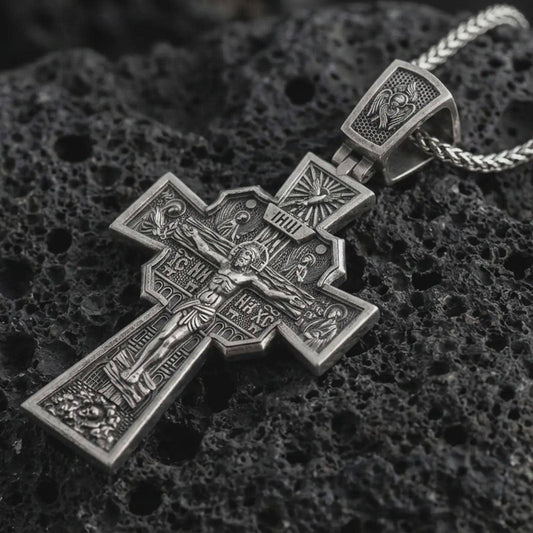 Sterling silver Orthodox cross pendant necklace with an oxidized finish resting on textured volcanic rock, captured in a close-up premium studio composition.