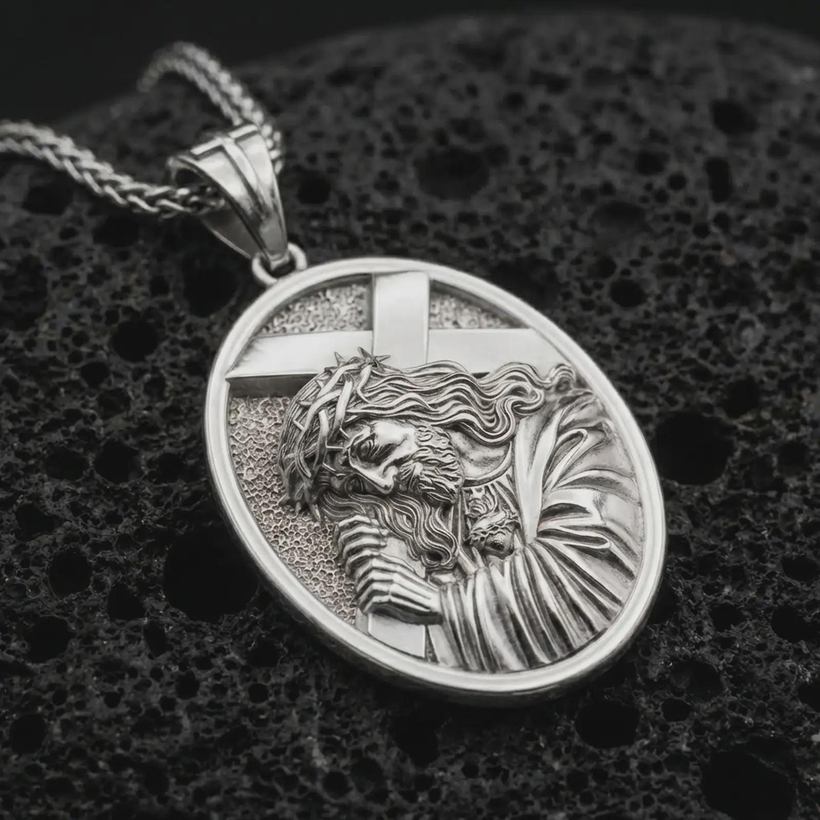 Polished silver Jesus carrying cross pendant necklace displayed on black volcanic rock, shown in a refined macro product shot with detailed sacred figure and cross relief.