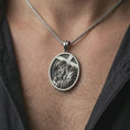 Load image into Gallery viewer, Oxidized Jesus carrying cross pendant necklace worn on the neck, styled in a dark lifestyle portrait with an open shirt and masculine presentation.
