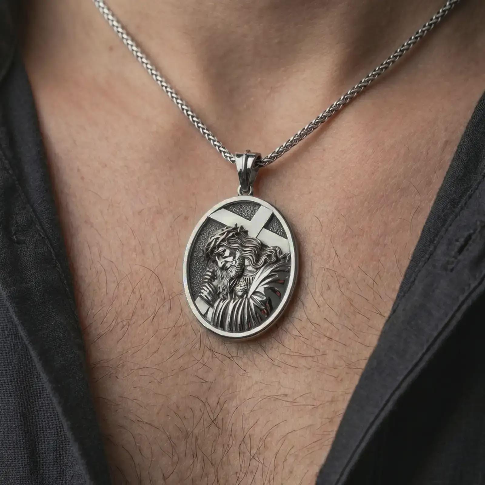 Oxidized Jesus carrying cross pendant necklace worn on the neck, styled in a dark lifestyle portrait with an open shirt and masculine presentation.