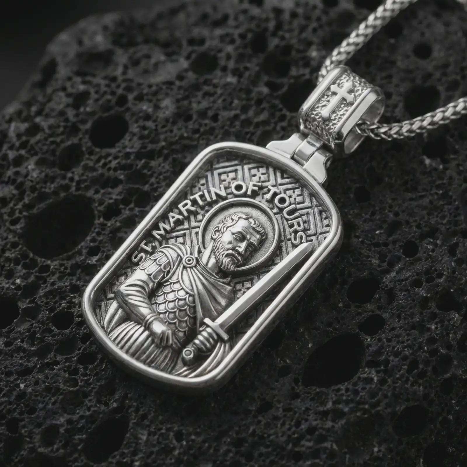 Polished silver Saint Martin of Tours pendant necklace displayed on black volcanic rock, shown in a refined macro product shot with detailed saint figure, sword, and engraved lettering.