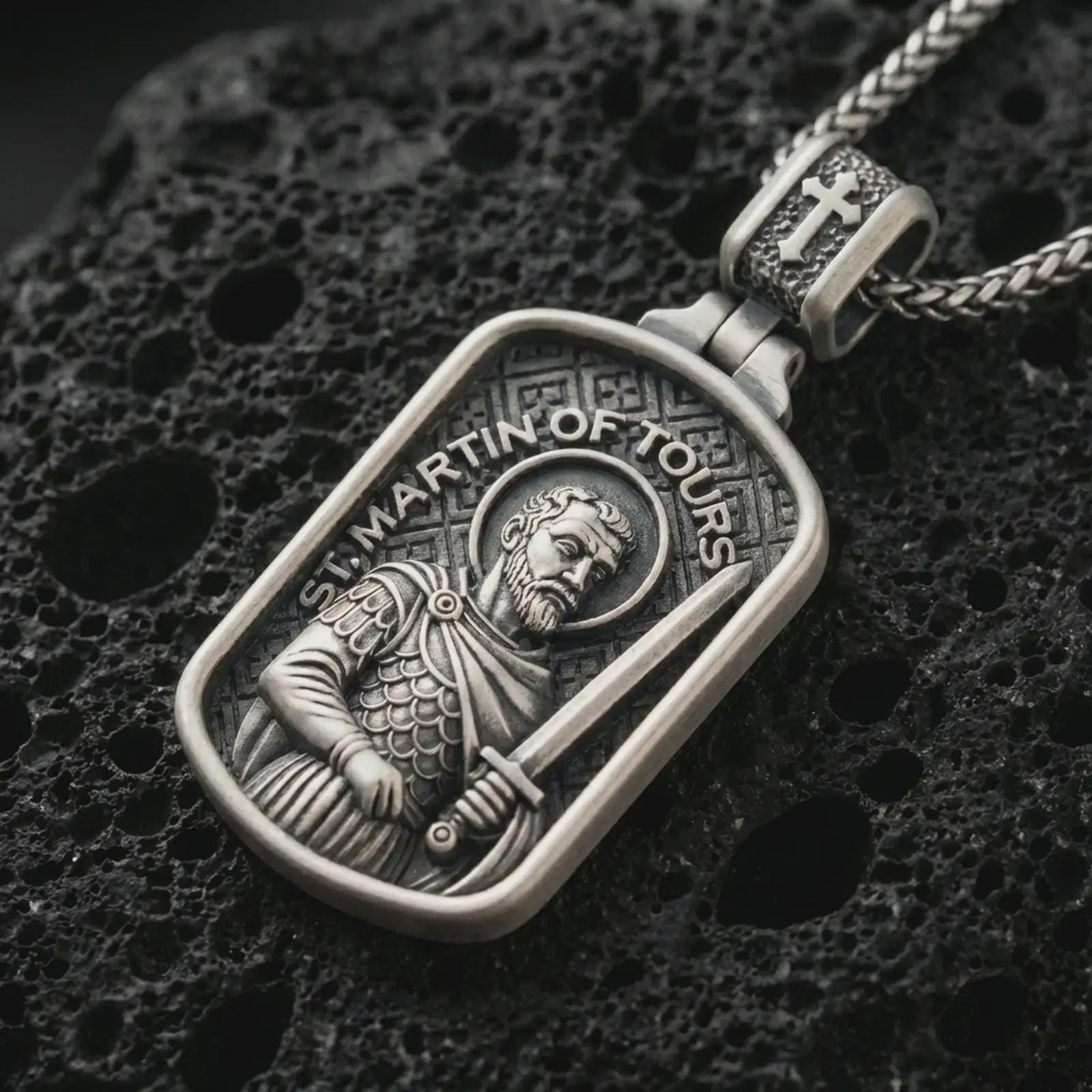 Sterling silver Saint Martin of Tours pendant necklace with an oxidized finish resting on textured volcanic rock, captured in a close-up premium studio composition.