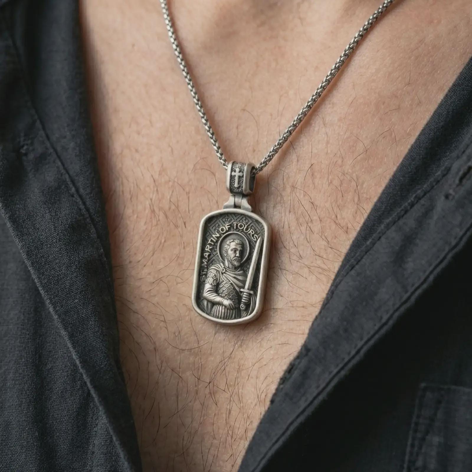 Oxidized Saint Martin of Tours pendant necklace worn on the neck, styled in a dark lifestyle portrait with an open shirt and masculine presentation.