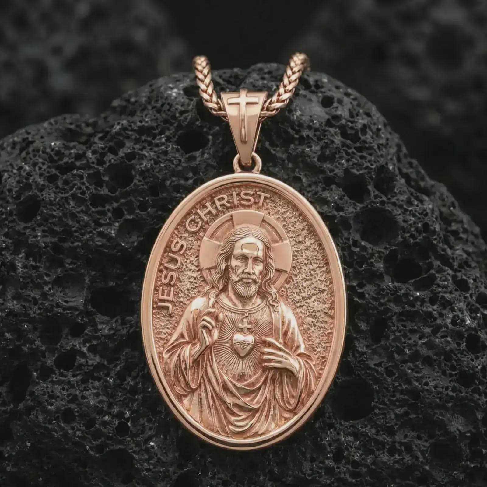 Rose gold plated Jesus Christ pendant necklace on dark volcanic rock, photographed in a detailed premium studio macro view.