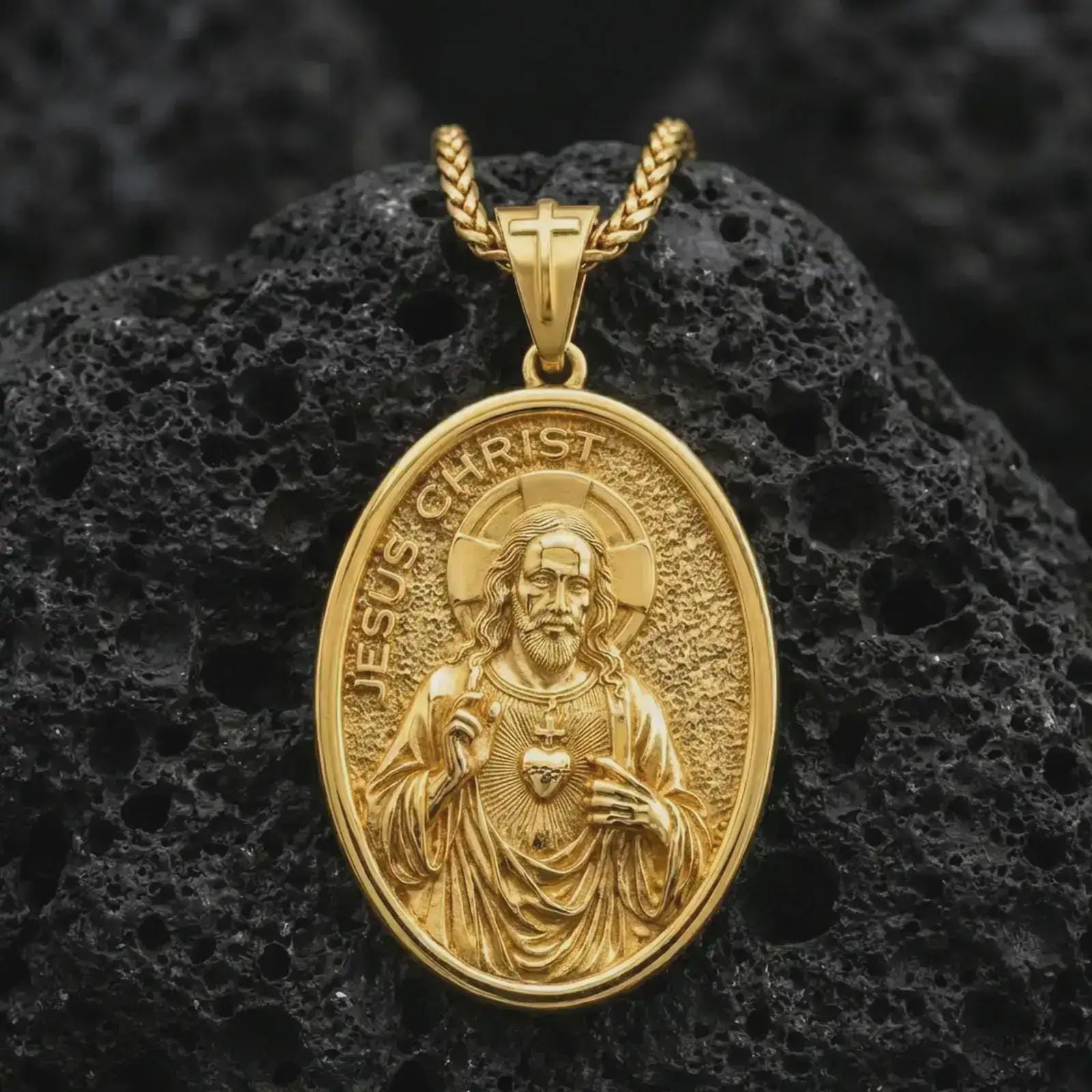 Gold plated Jesus Christ pendant necklace presented on porous volcanic rock, highlighting the oval medallion form and devotional heart motif in a luxurious close-up jewelry image.