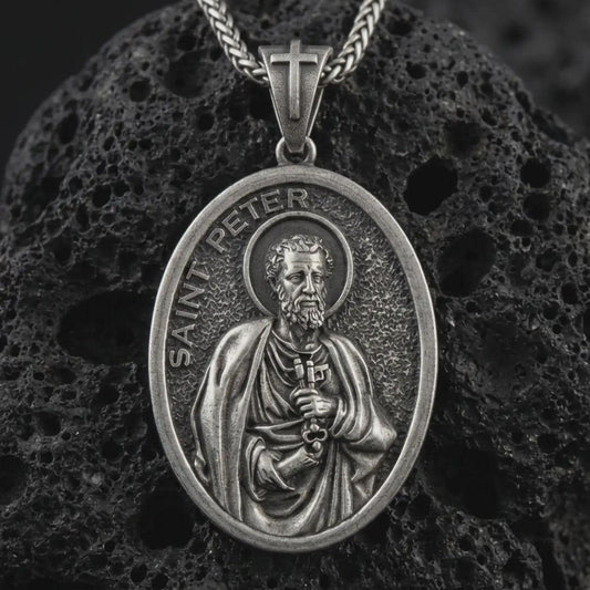 Sterling silver Saint Peter pendant necklace with an oxidized finish resting on textured volcanic rock, captured in a close-up premium studio composition.