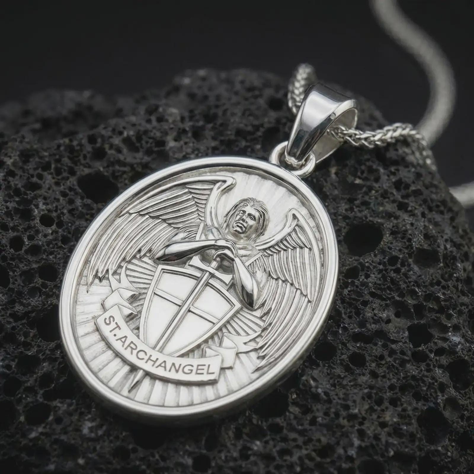 Polished silver Saint Michael Archangel pendant necklace displayed on black volcanic rock, shown in a refined macro product shot with detailed winged guardian figure and shield relief.