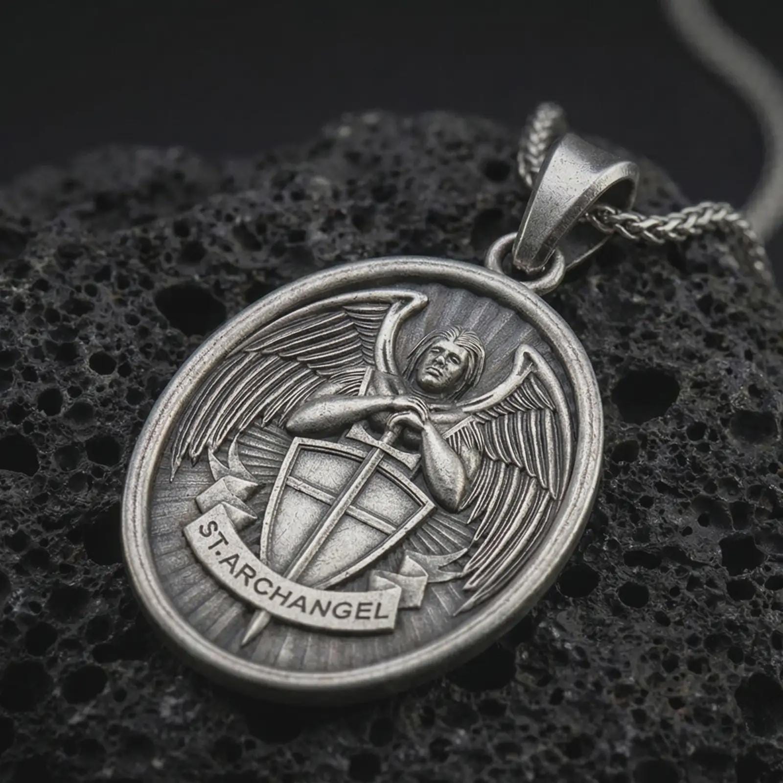 Sterling silver Saint Michael Archangel pendant necklace with an oxidized finish resting on textured volcanic rock, captured in a close-up premium studio composition.