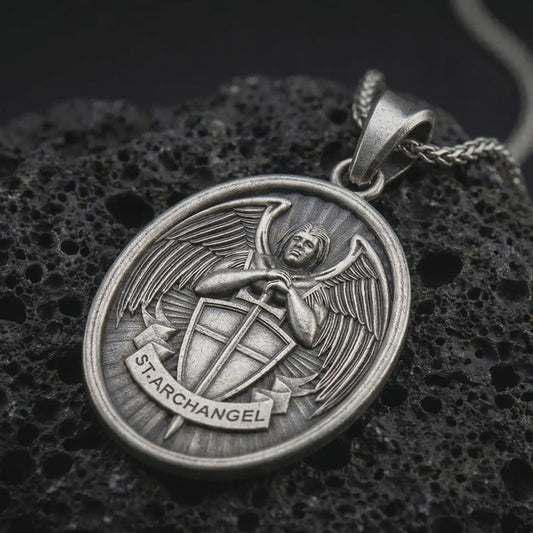 Sterling silver Saint Michael Archangel pendant necklace with an oxidized finish resting on textured volcanic rock, captured in a close-up premium studio composition.