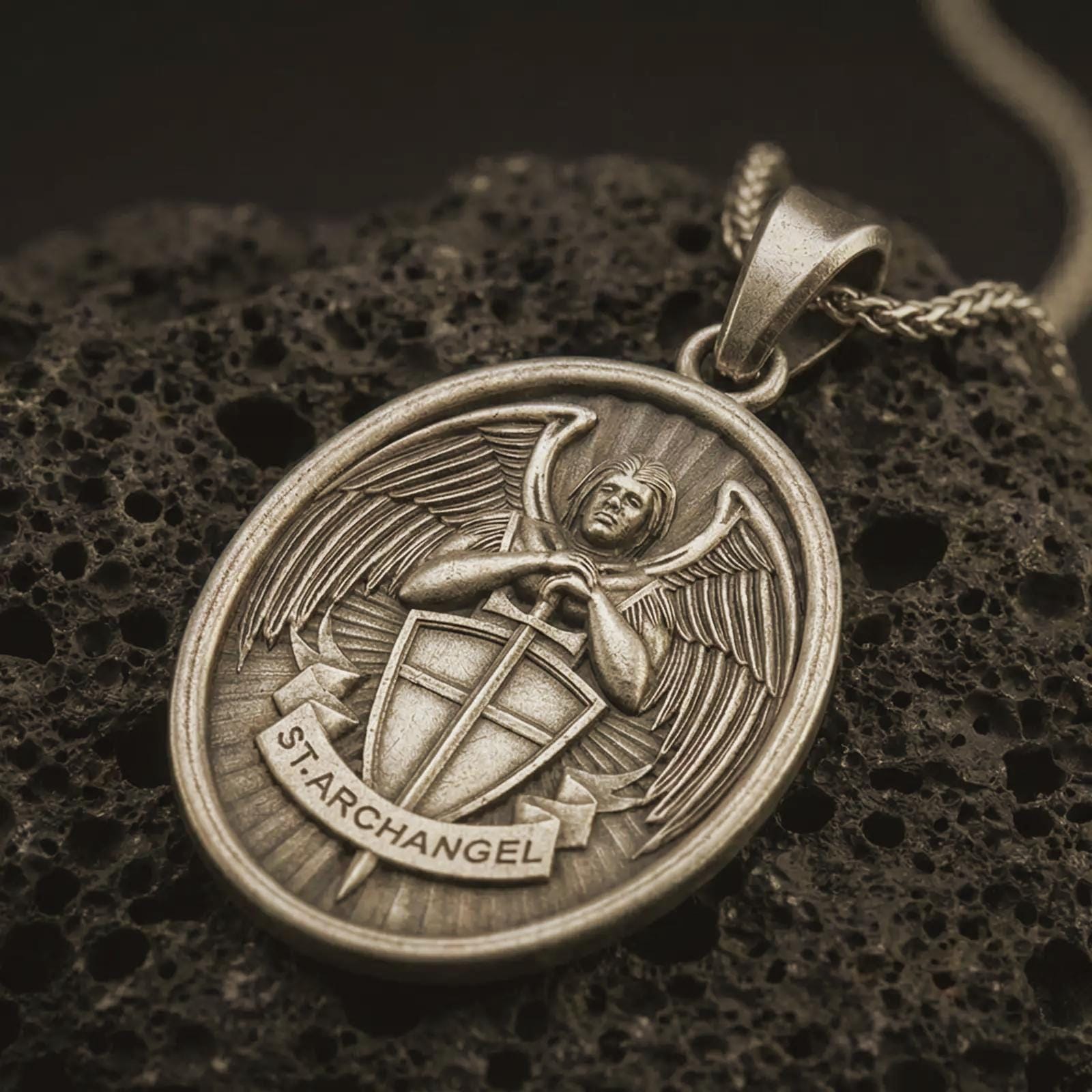 Bronze Saint Michael Archangel pendant necklace with an oxidized finish resting on textured volcanic rock, captured in a close-up premium studio composition.