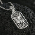 Load image into Gallery viewer, Polished silver Saint George dog tag pendant necklace displayed on black volcanic rock, shown in a refined macro product shot with detailed mounted saint and dragon slayer relief.
