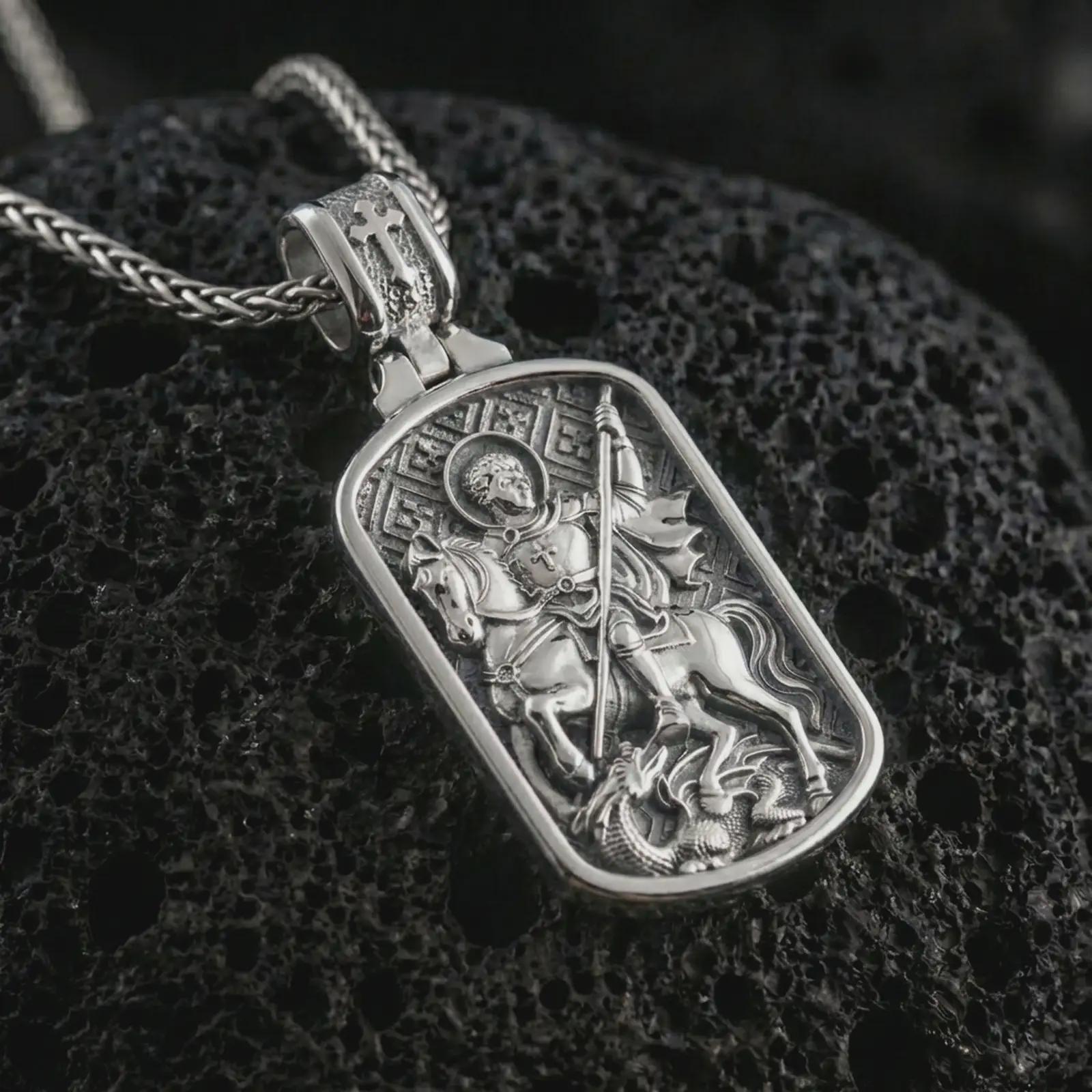 Polished silver Saint George dog tag pendant necklace displayed on black volcanic rock, shown in a refined macro product shot with detailed mounted saint and dragon slayer relief.
