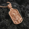 Load image into Gallery viewer, Rose gold plated Saint Benedict dog tag pendant necklace on dark volcanic rock, photographed in a detailed premium studio macro view.

