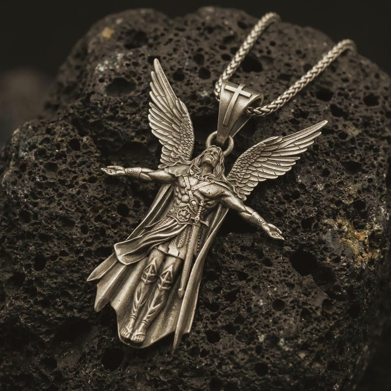 Bronze Archangel Michael pendant necklace with an oxidized finish resting on textured volcanic rock, captured in a close-up premium studio composition.
