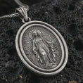 Load image into Gallery viewer, Sterling silver Miraculous Medal pendant necklace with an oxidized finish resting on textured volcanic rock, captured in a close-up premium studio composition.
