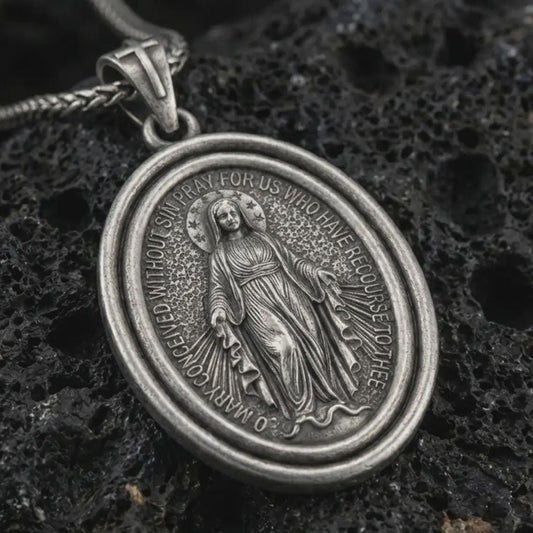 Sterling silver Miraculous Medal pendant necklace with an oxidized finish resting on textured volcanic rock, captured in a close-up premium studio composition.