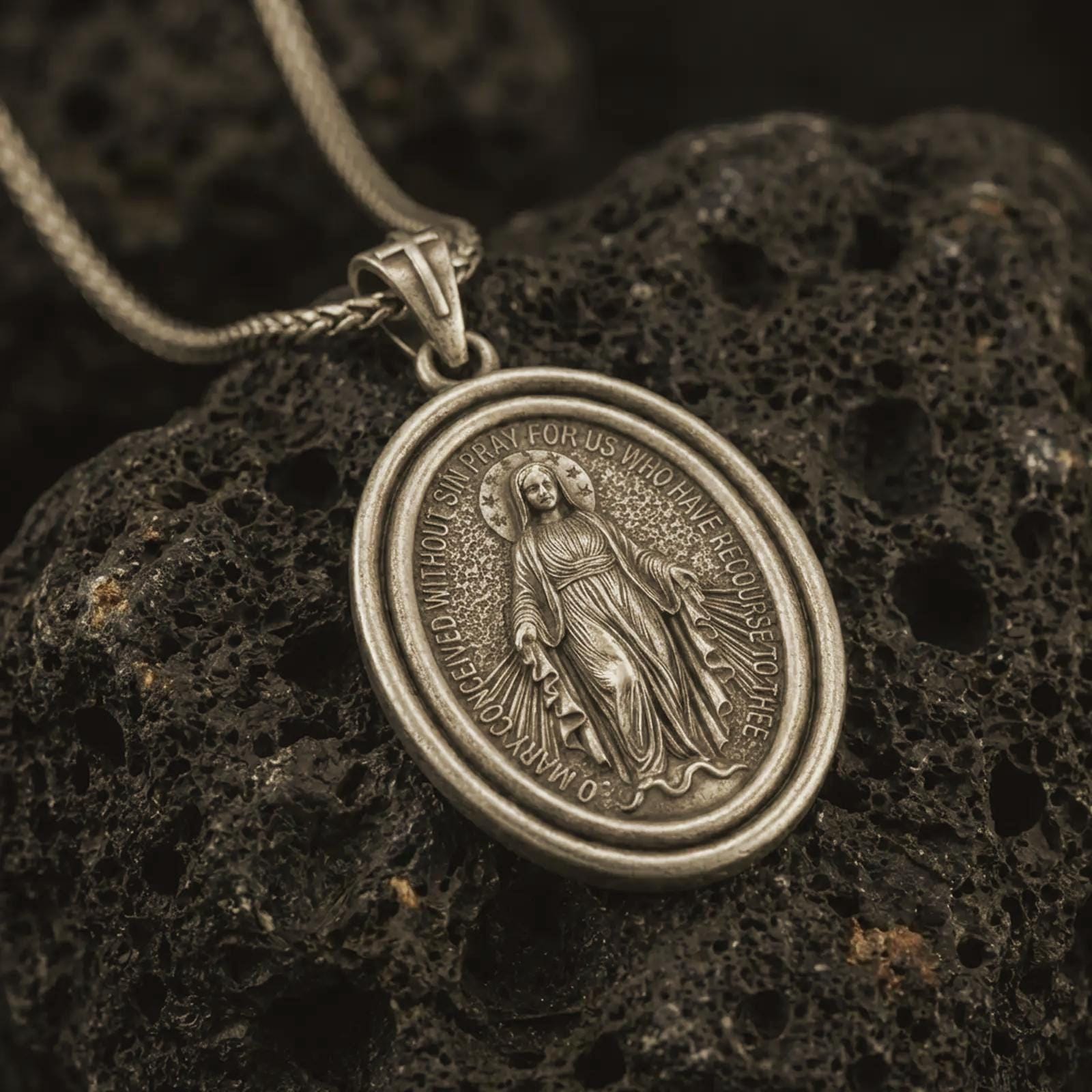 Bronze Miraculous Medal pendant necklace with an oxidized finish resting on textured volcanic rock, captured in a close-up premium studio composition.