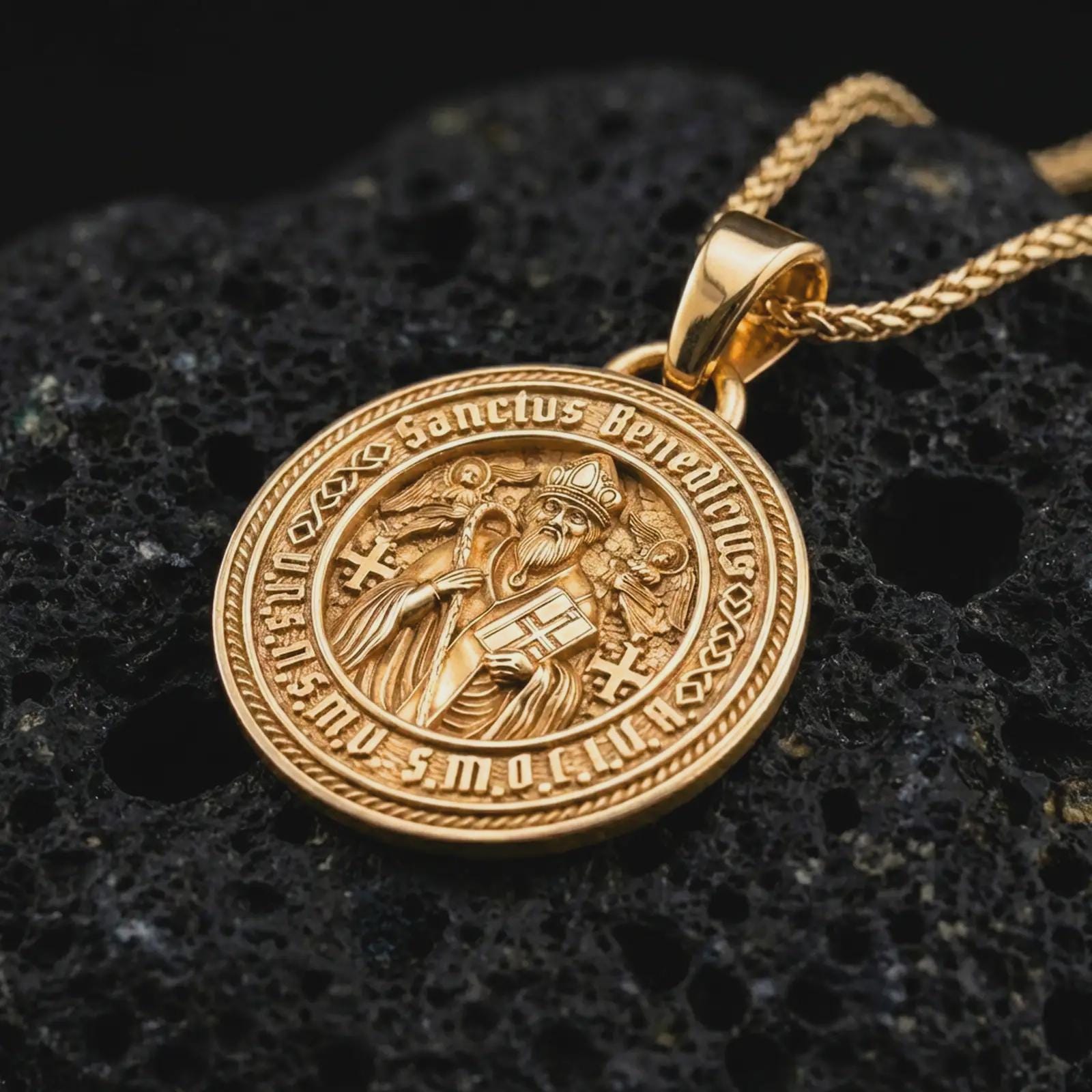 Gold plated Saint Benedict medal pendant necklace presented on porous volcanic rock, highlighting the round devotional medallion design in a luxurious close-up jewelry image.