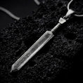 Load image into Gallery viewer, Sterling silver Dragonslayer sword pendant necklace with an oxidized finish resting on textured volcanic rock, captured in a close-up premium studio composition.
