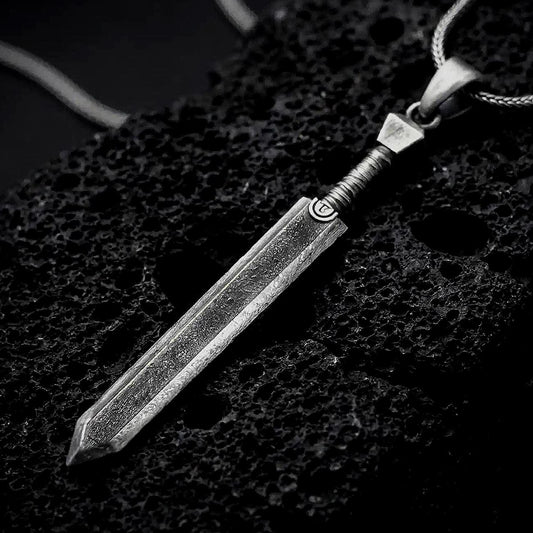 Sterling silver Dragonslayer sword pendant necklace with an oxidized finish resting on textured volcanic rock, captured in a close-up premium studio composition.