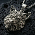 Load image into Gallery viewer, Oxidized wolf head pendant with intricate carved fur details and fierce animal expression displayed on dark volcanic rock in a close-up luxury jewelry composition
