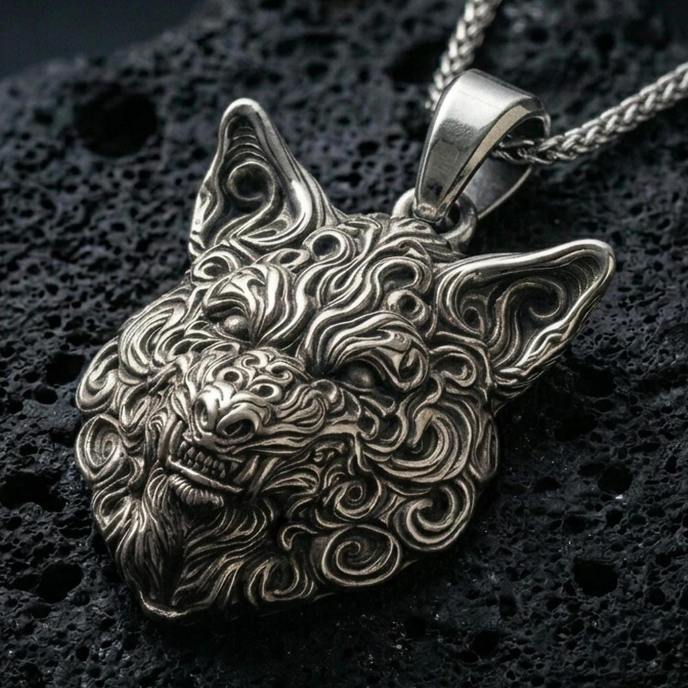 Oxidized wolf head pendant with intricate carved fur details and fierce animal expression displayed on dark volcanic rock in a close-up luxury jewelry composition