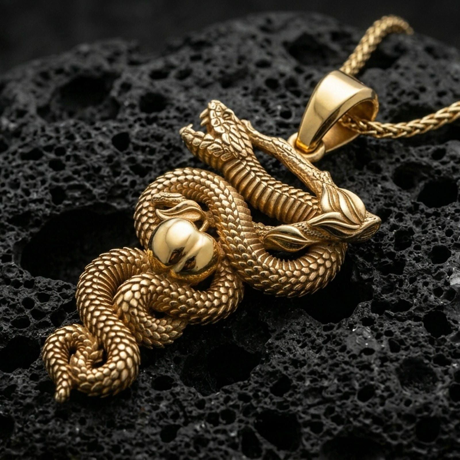 Gold plated serpent pendant with coiled snake body, realistic scale relief, apple motif, and symbolic branch detail showcased on black volcanic rock in a refined macro jewelry image