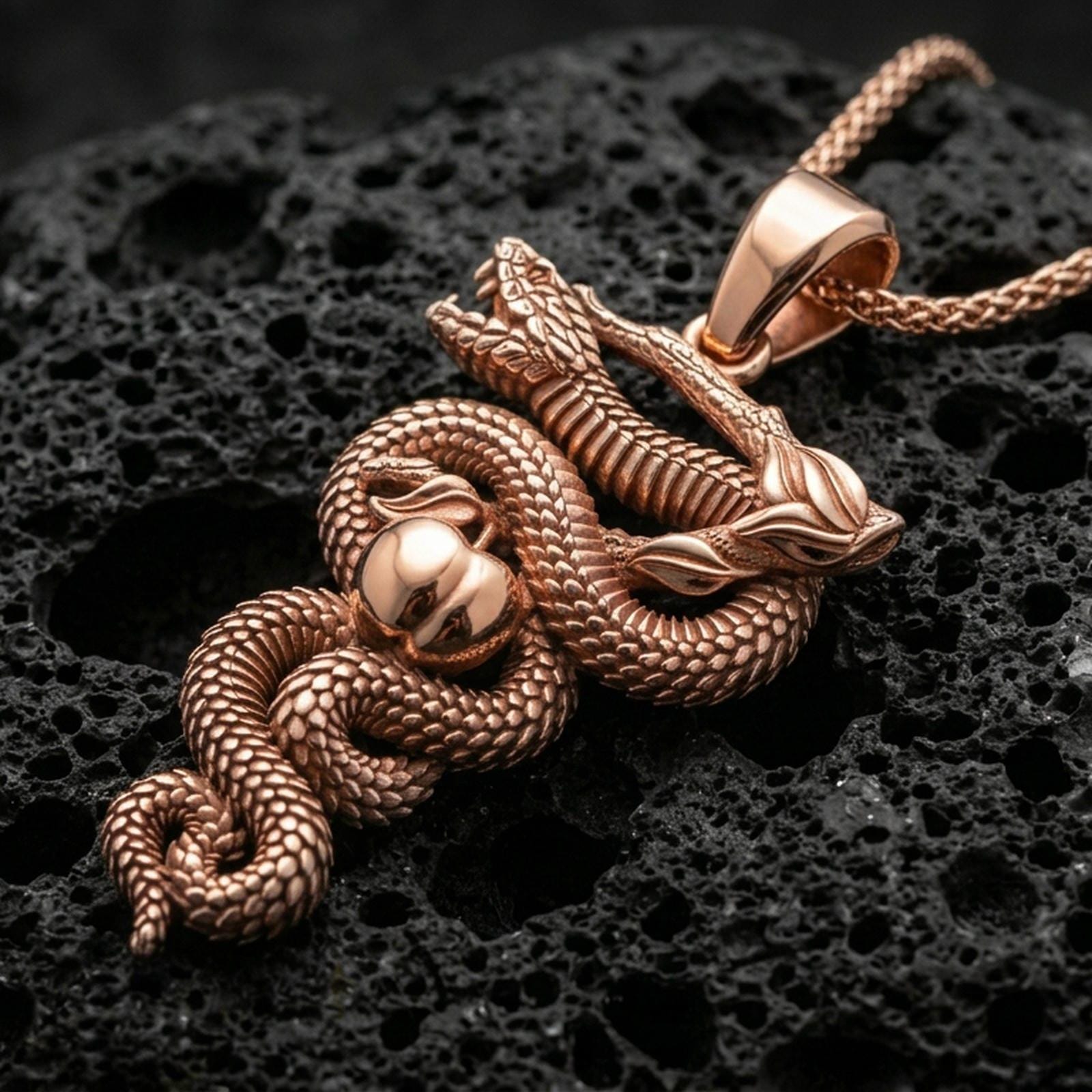 Rose gold plated snake pendant with wrapped serpent silhouette, textured scales, apple element, and detailed organic branch design resting on volcanic rock in an elegant close-up product presentation