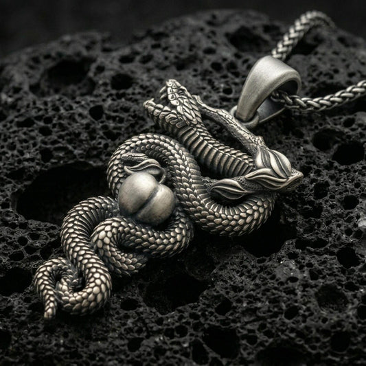 Oxidized serpent pendant with coiled snake, apple detail, and branch motif displayed on dark volcanic rock in a close-up luxury jewelry composition