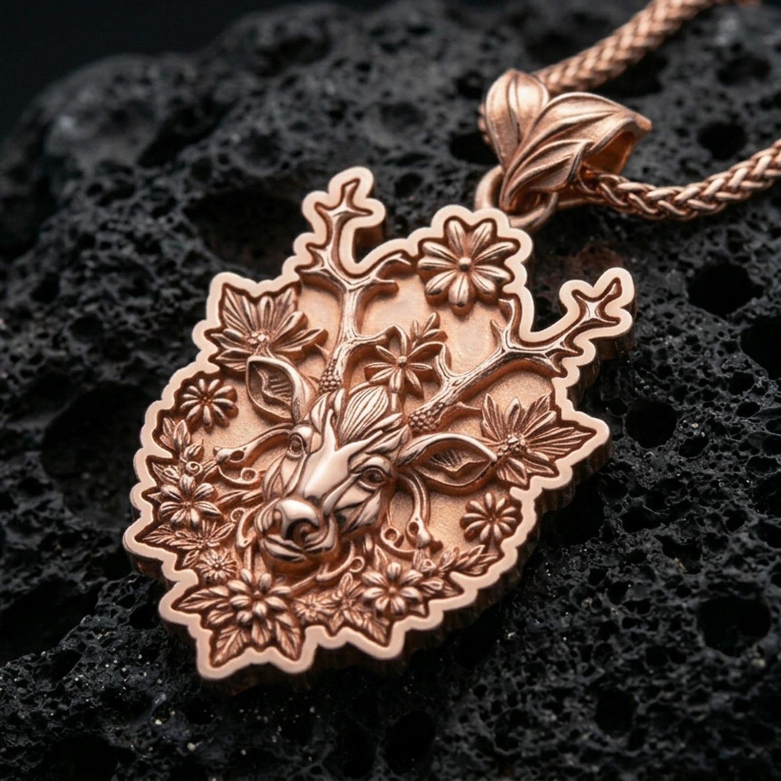 Rose gold plated stag pendant with flower-adorned antlers, intricate botanical detailing, and elegant woodland silhouette resting on volcanic rock in an elegant close-up product presentation
