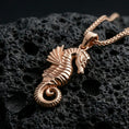 Load image into Gallery viewer, Rose gold plated seahorse pendant with detailed body relief, curled tail, and graceful nautical form resting on volcanic rock in an elegant close-up product presentation
